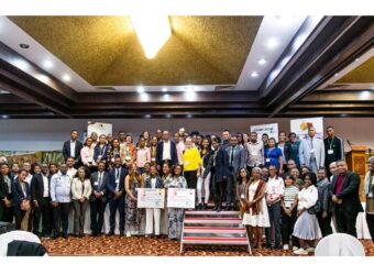 Conference participants gather on a stage and pose together for a group photo.