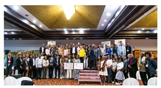 Conference participants gather on a stage and pose together for a group photo.