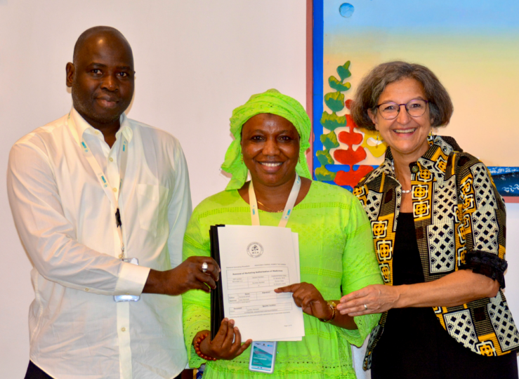 Group photo with three people smiling for the camera. The person in the middle is holding a document in their hand.