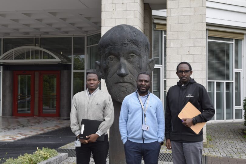 Group photo in front of the entrance of the Paul-Ehrlich-Institut building. The three people in the picture are posing in front of the bust of Paul Ehrlich.