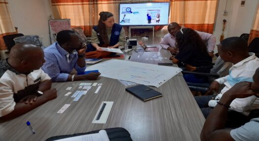 Eine Gruppen von Personen sitzt an einem Seminartisch, auf welchem ein beschriebenes Flipchart-Papier liegt.