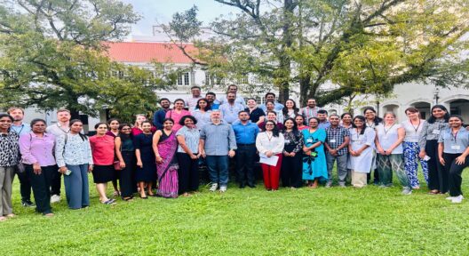 Gruppenfoto auf einer Wiese im Freien. Im Hintergrund befindet sich eine Art Institutsgebäude