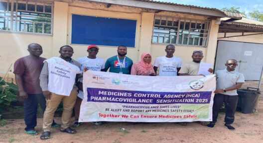Eine Gruppe von Personen steht vor einem Gebäude und hält ein Banner mit Aufschrift: "Medicines Control Agency - Pharmacovigilance Sensitizateion 2025""