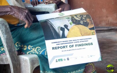 The hands and lap of an older seated woman holding a spiral-bound document. The document includes the text “Report of Findings” and a sentence in Igbo language.