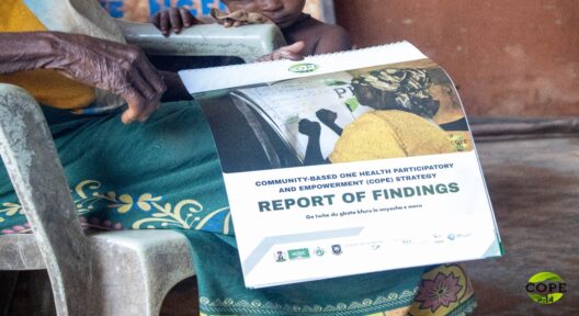 Bildausschnitt: Hände und Schoß einer älteren, sitzenden Frau, die ein ein Dokument mit Spiralbindung in den Händen hält. Auf den Dokument steht u.a. "Report of Findings" und ein Satz in einem Idgbo-Dialekt